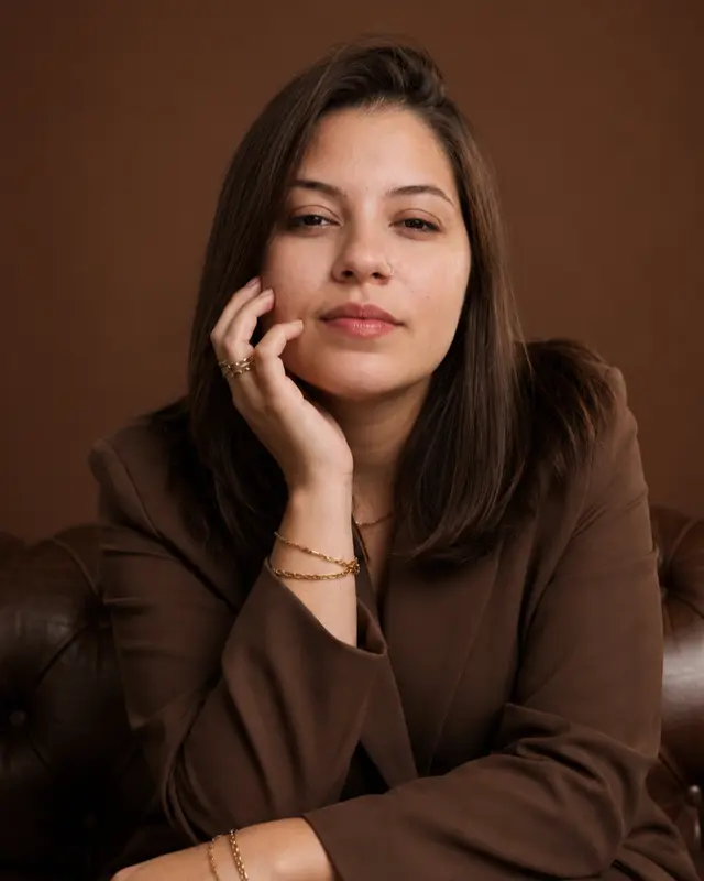 Retrato de Gabriela Pantarotto, de blazer marrom, sentada em um sofá de couro, com a mão apoiada no rosto